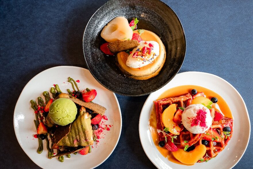 Overhead view of three plates of breakfast food, including waffles, poached fruits, and pancakes.