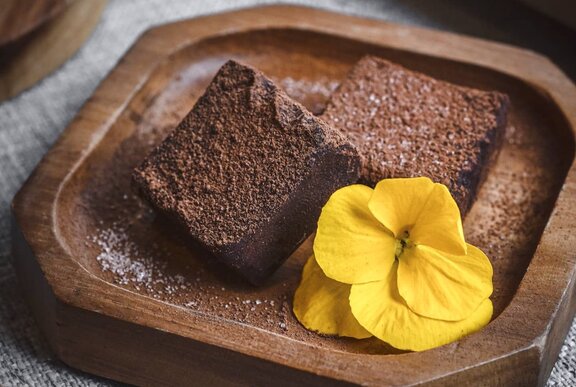 Two squares of fudgy chocolate cake on a small wooden plate with a yellow flower garnish.