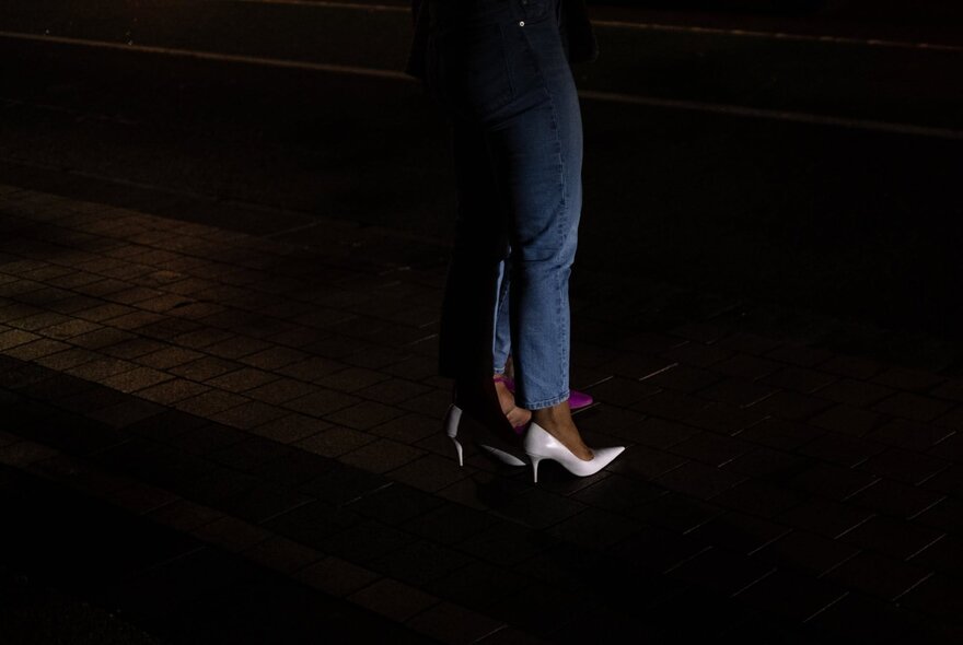 A woman's legs and high heeled shoes, on the street at night.