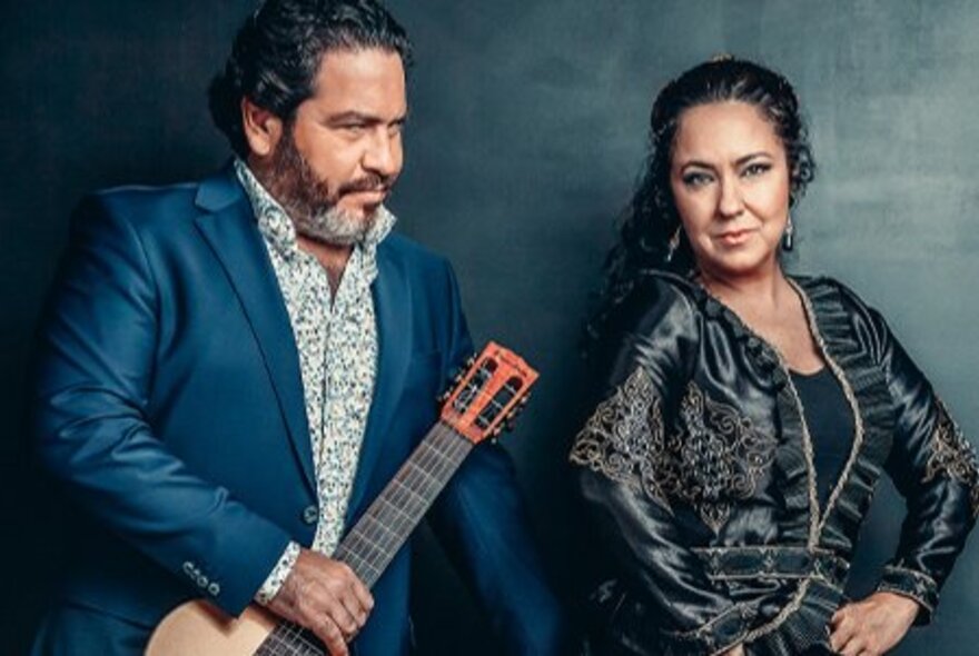 Flamenco guitarist with beard holding guitar, next to dancer with her hands on her hips.