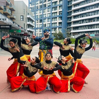 A group of dancers performing a lively, synchronised choreography outdoors in traditional-inspired performance attire.