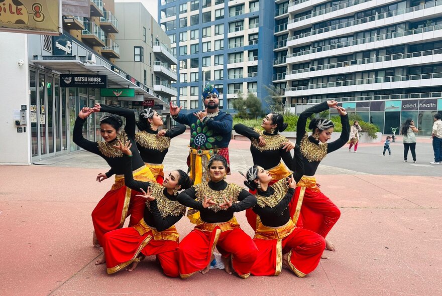 A group of dancers performing a lively, synchronised choreography outdoors in traditional-inspired performance attire.
