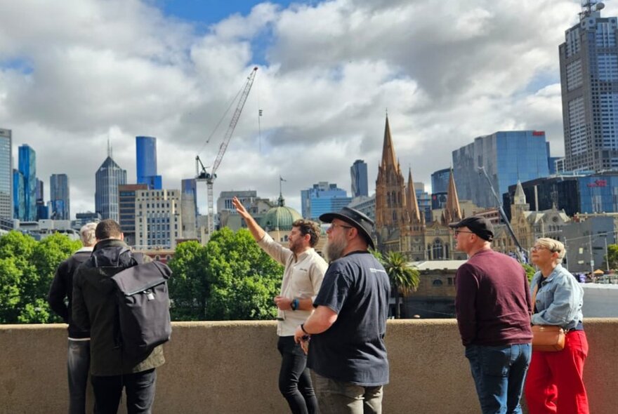 A group of people on a high outdoor balcony with one man pointing and others looking in that direction. 