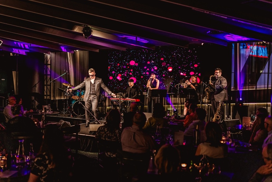A singer and band performing live on a stage inside Amphora restaurant, with patrons seated at dining tables watching the show.