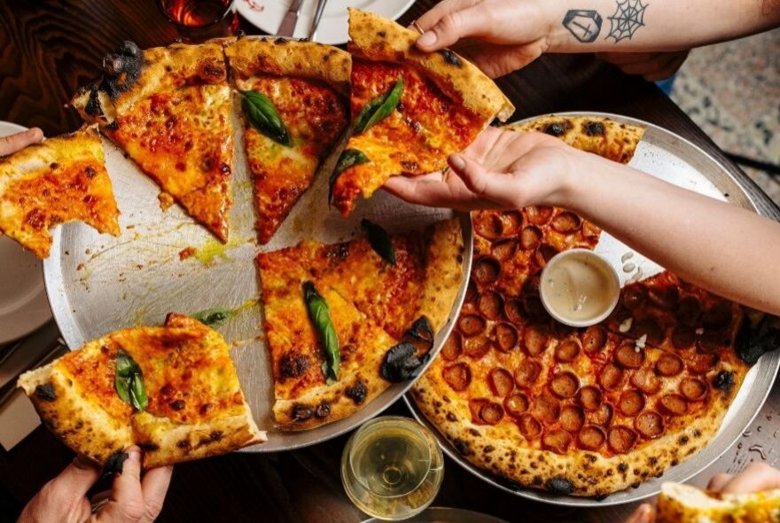 Hands grabbing pizza slices on a table. 