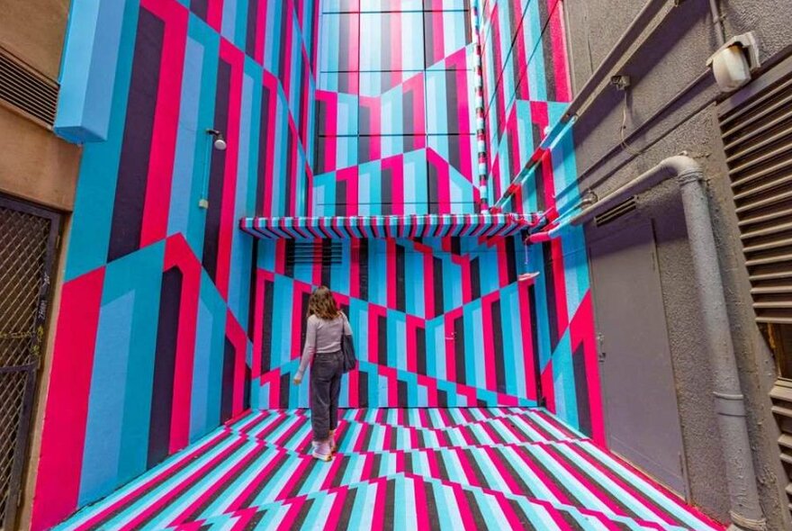 A woman standing in front of a tall mural in a laneway