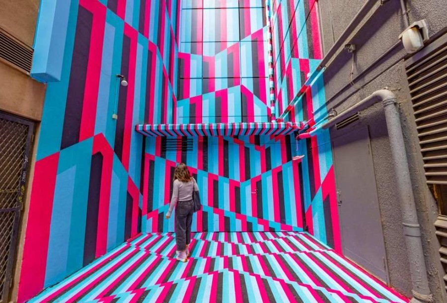 A woman standing in front of a tall mural in a laneway