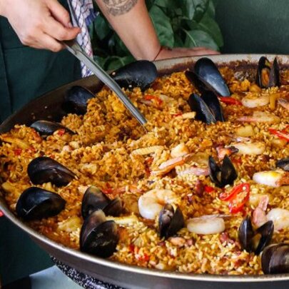 Person stirring large pan of seafood paella.