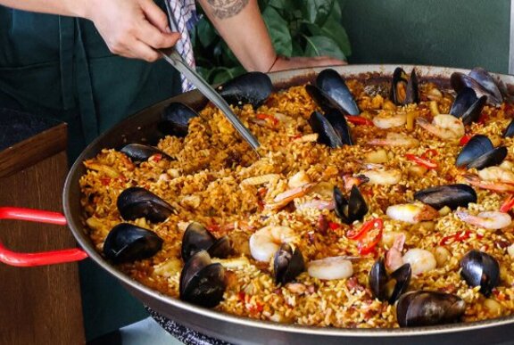Person stirring large pan of seafood paella.
