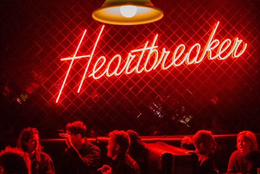 People sitting at tables and booths at Heartbreaker Bar, with a neon red Heartbreaker sign on the wall.