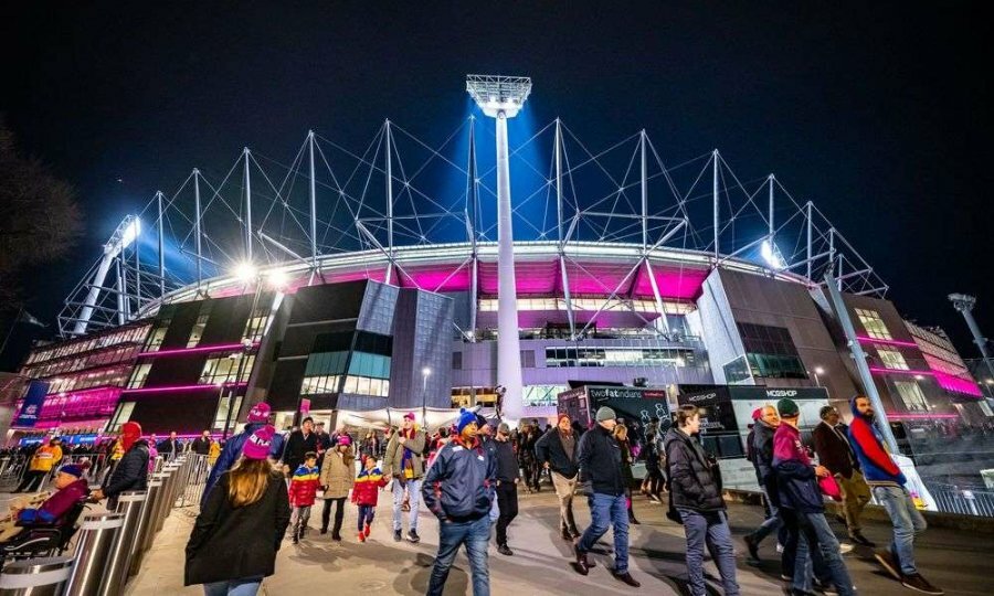 People walking beneath a large sports stadium at night