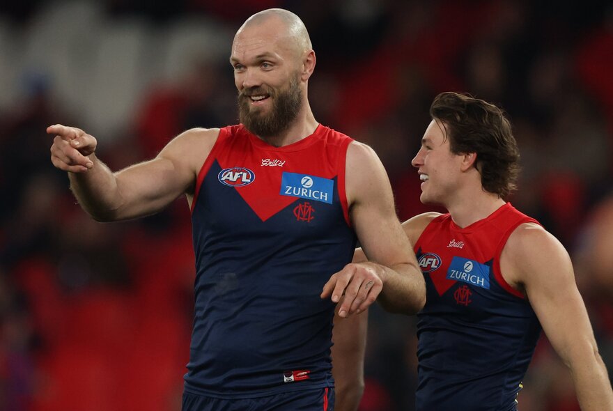 Two Melbourne AFL players smiling on the football field, one of them pointing.