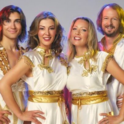 ABBA tribute band BABBA dressed in white and gold tunics with their hands on their hips.
