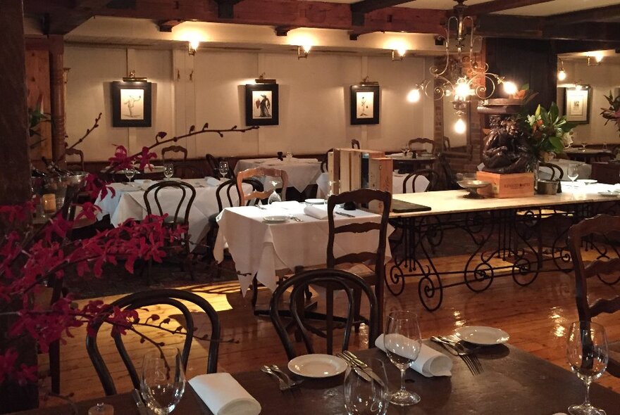 The basement dining room of Caterina's restaurant with warm and soft lighting, tables set for service, and small spotlit paintings on the walls. 