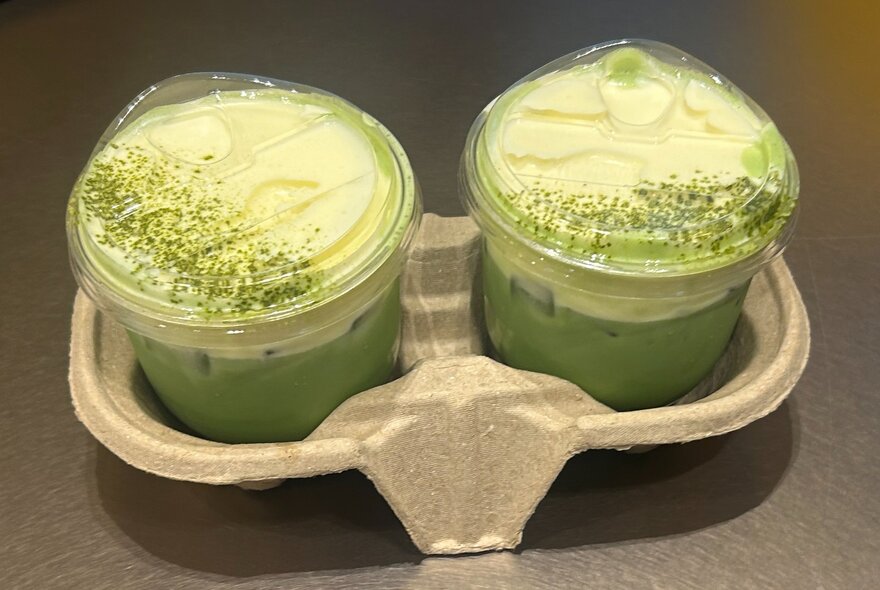 Two clear takeaway cups in a cardboard cup holder with ceremonial matcha and Bhutanese buttercream on top.