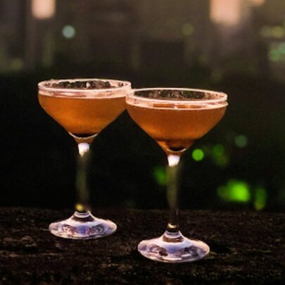 Two pink cocktail glasses on a dark bench.