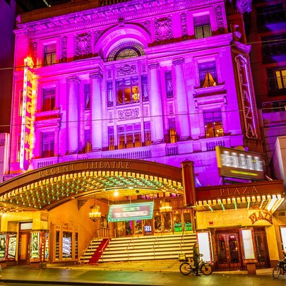 The exterior of a city theatre lit up pink at night.