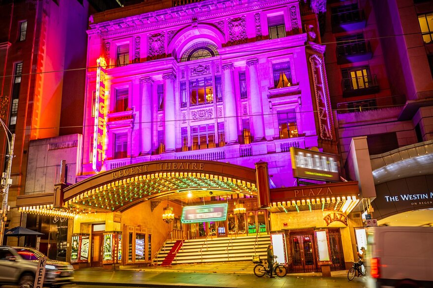 The exterior of a city theatre lit up pink at night.