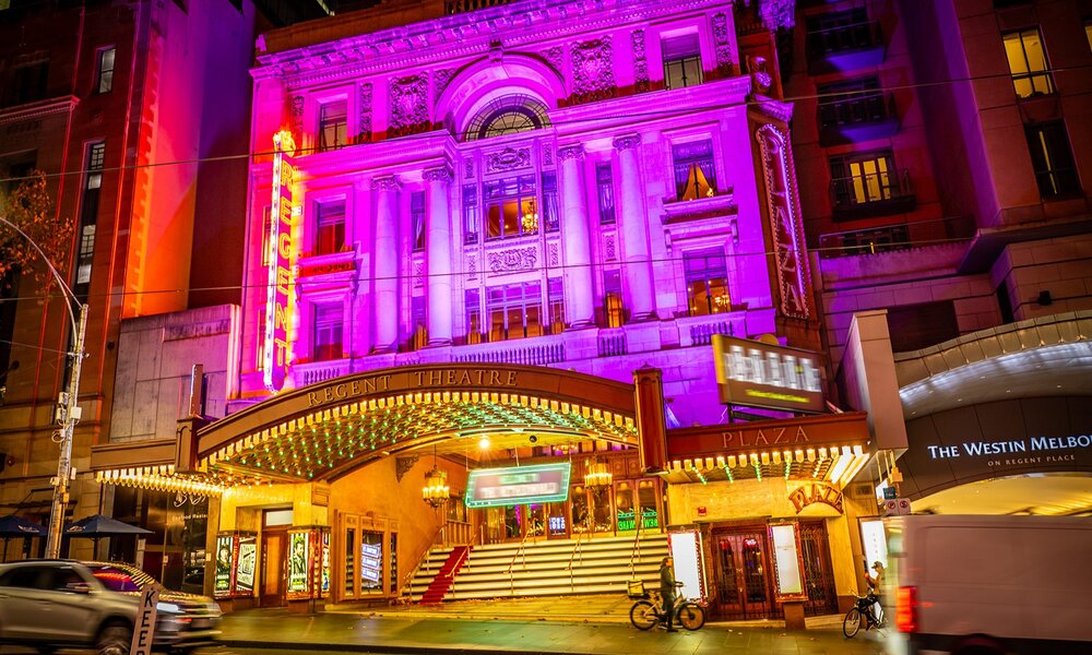 The exterior of a city theatre lit up pink at night.