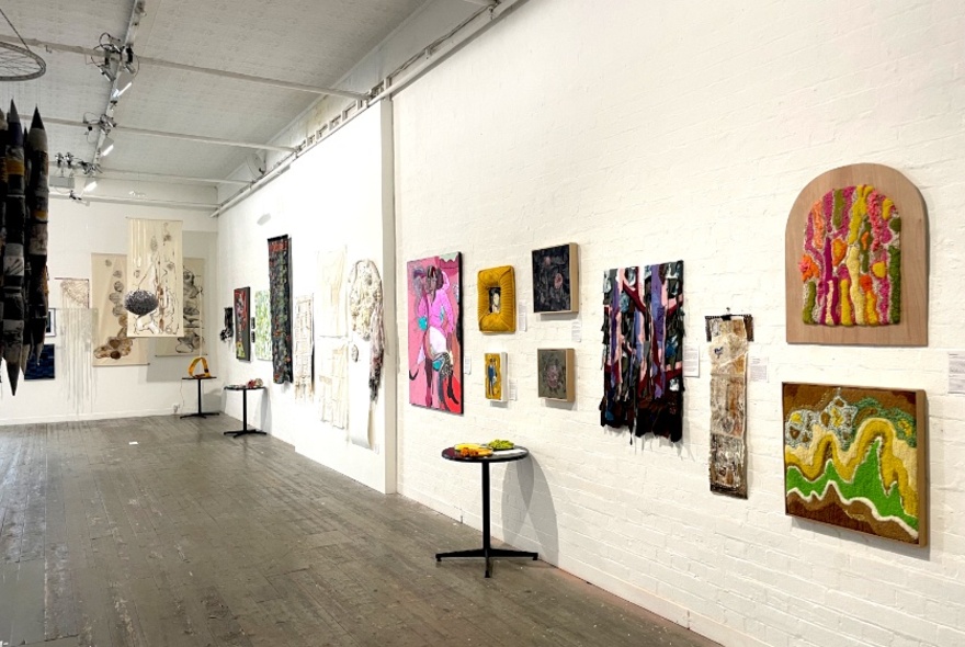 An exhibition of textiles in a gallery setting, arranged on the white walls.