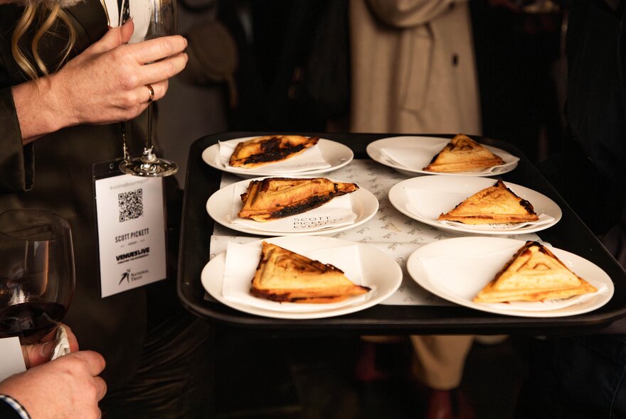 People selecting from a tray of toasted sandwiches.