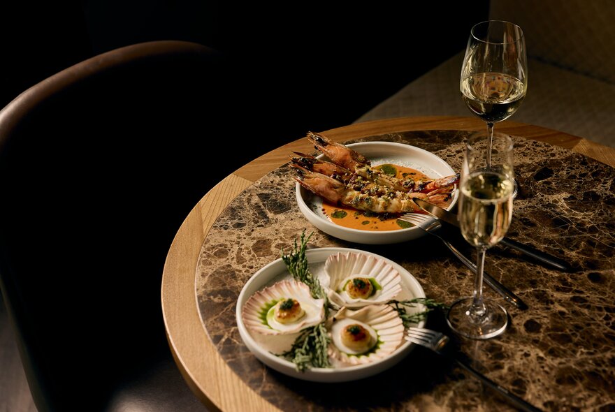 A table setting with two glasses of white wine paired with two seafood dishes.