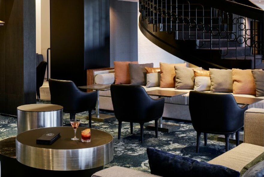 Interior of Cliveden restaurant showing lounge seating with small tables and occasional chairs, a low round coffee table, and a curved staircase in the background.