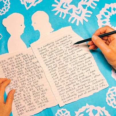Hands holding a black pen over two pages of writing on pieces of paper with figure cutouts.