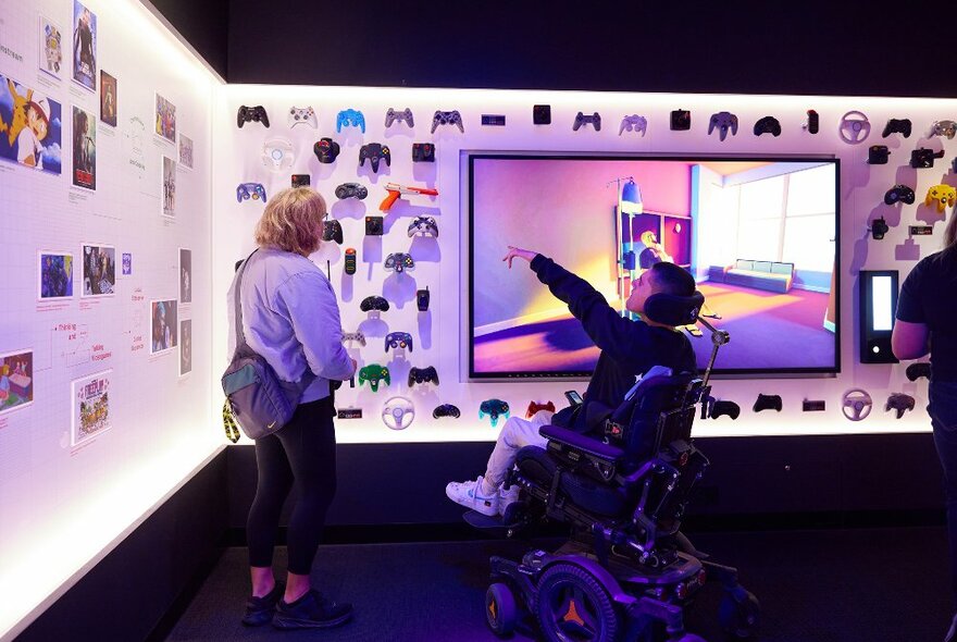 A mother and son are looking at an exhibition display of retro game consoles