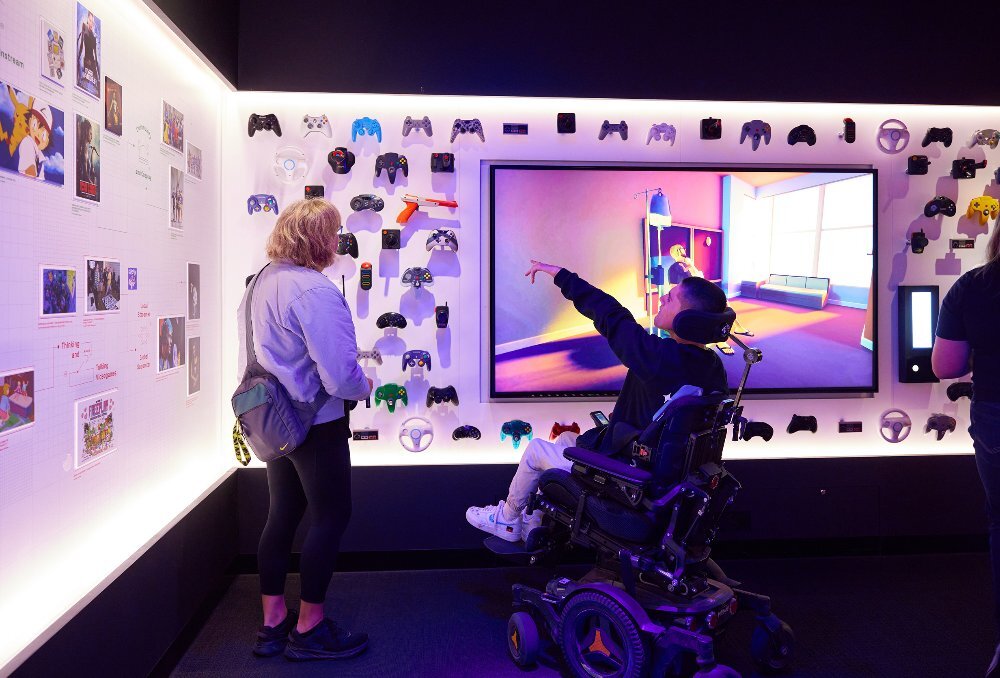 A mother and son are looking at an exhibition display of retro game consoles