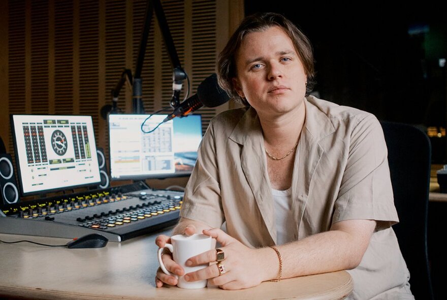 A person wearing a beige shirt, hands around a mug of coffee, in a sound studio.