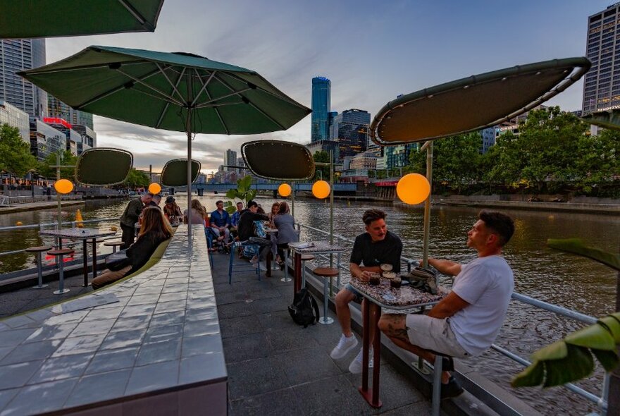 Twilight view from Ponyfish Island Bar showing two men drinking at a table in the right foreground with other people seated in the background.