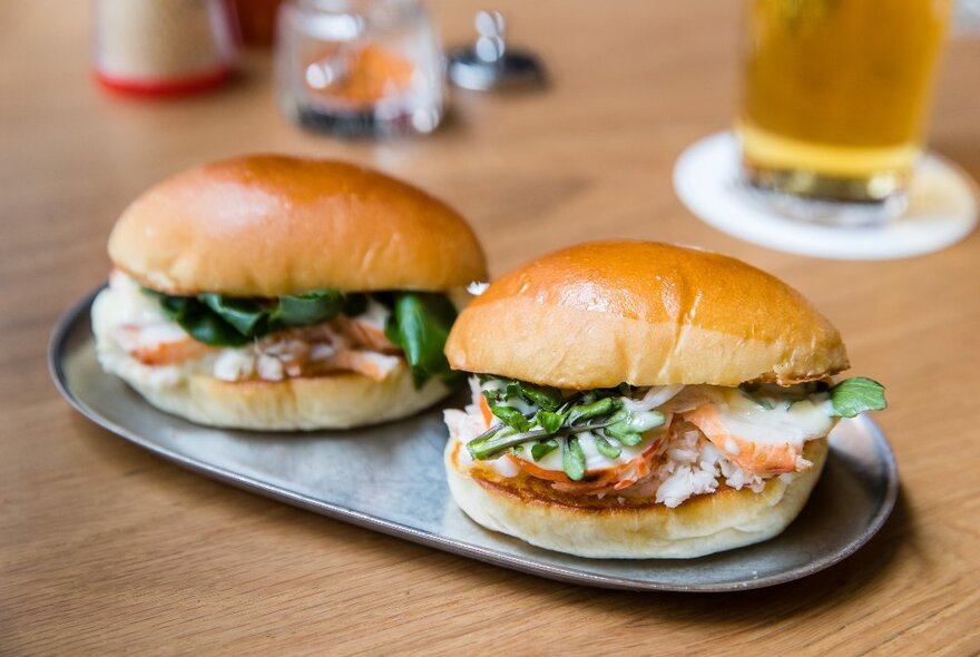 Two lobster rolls on a small silver tray.