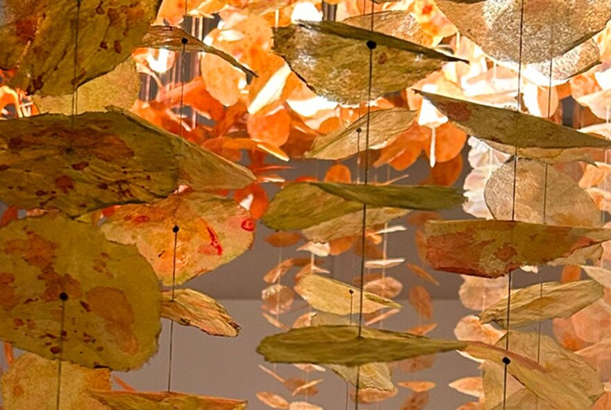 An art installation of hanging pieces of stiff paper of natural hues, threaded onto strings that hang vertically.