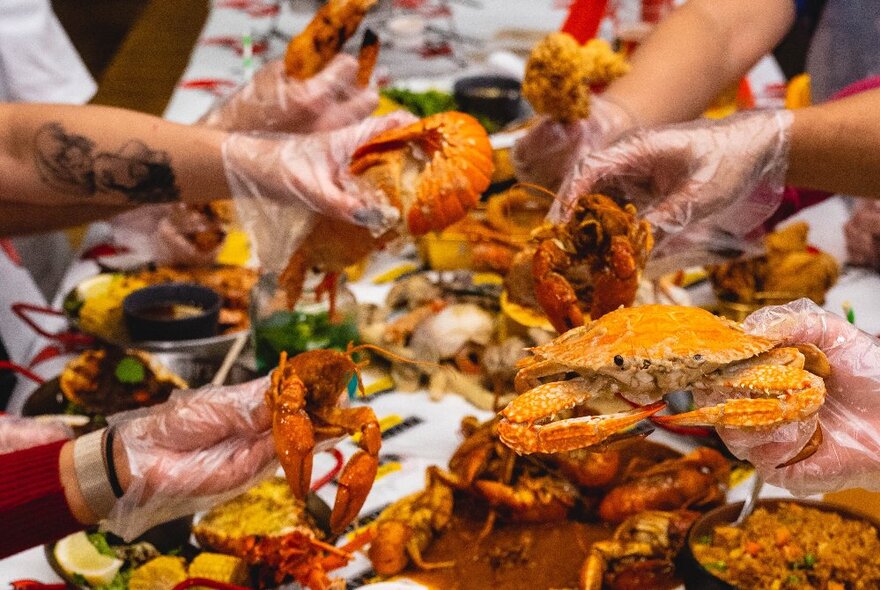 Hands wearing plastic gloves picking up fried seafood from a restaurant table.