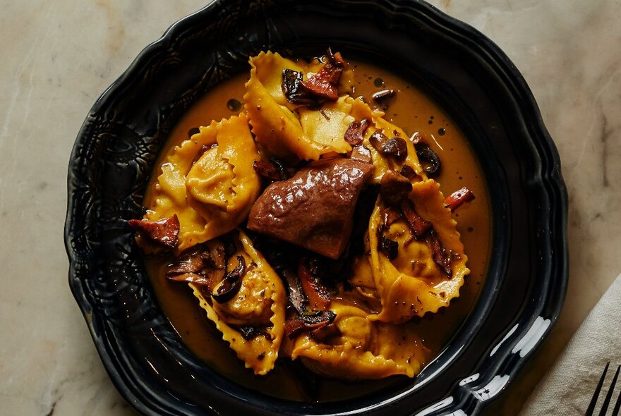 Looking down at a bowl of filled pasta, resting in a rich dark sauce.