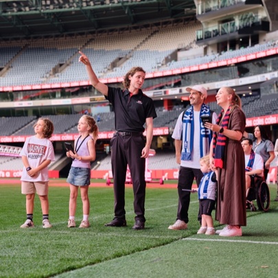 A tour guide with a family of five, pointing upwards to the stands at Marvel Stadium.