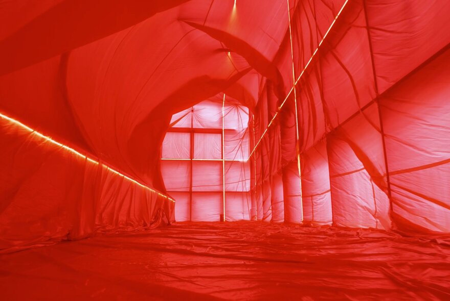 Pink-hued translucent fabric installation, lining the internal walls and ceiling of a building.
