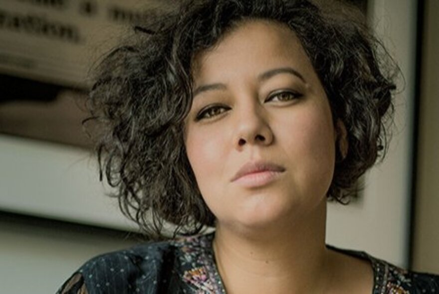 Close up head shot of singer Mahalia Barnes, with a neutral expression and short wavy dark hair.