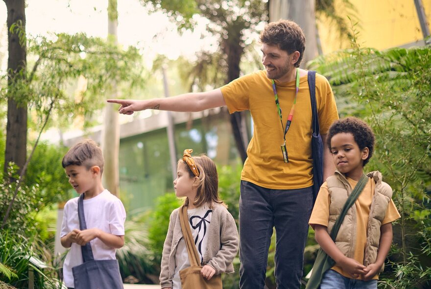 Three children and an adult in a garden, the adult pointing at a tree.