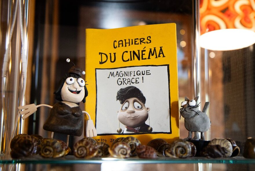 Stop-motion figurines on a glass shelf with movie poster, mirror and patterned lightshade.