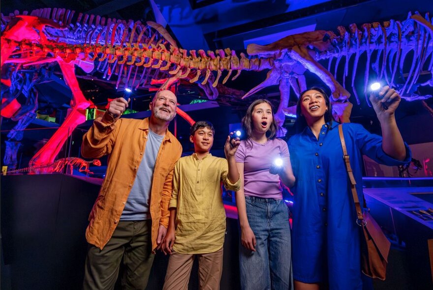 A family of four standing in a neon-lit museum gallery with a dinosaur skeleton.