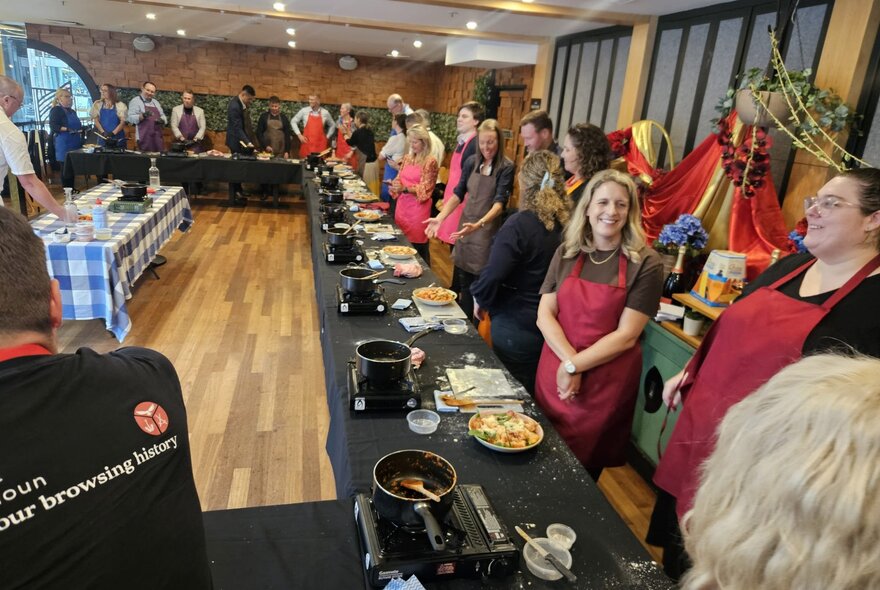 Participants standing behind tables with portable stoves and cooking implements in a restaurant setting.