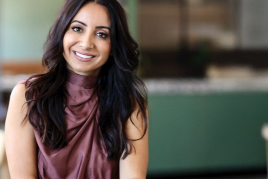 Journalist Antoinette Lattouf smiling warmly with her long dark hair hanging down over a sleeveless purple top. 