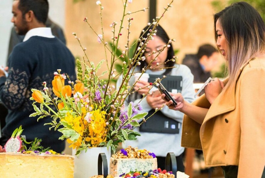 A woman taking a picture of a floral arrangement on her phone.