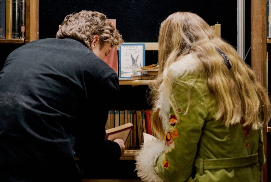 Two people hunched over a shelf looking at books, seen from behind, at a rare book fair.
