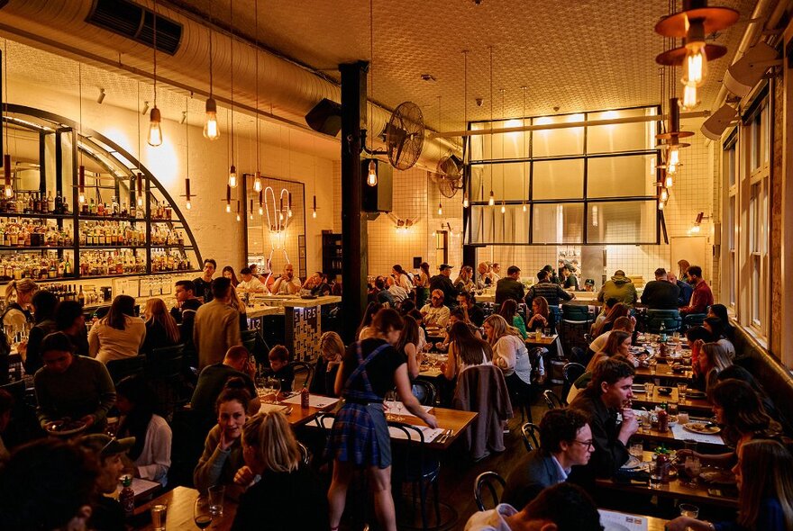 Interior of Chin Chin restaurant, filled with patrons seated at dining tables, high ceilings giving an industrial warehouse feel to the busy space. 