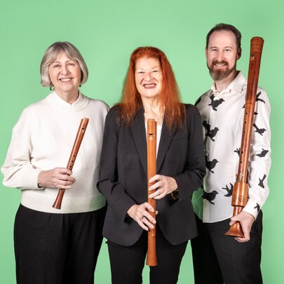 Three musicians smiling against a green background, each holding a wooden recorder of a different size.