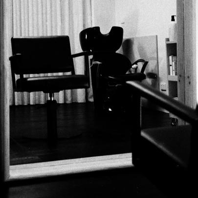 Black and white shot of an empty hair salon chair in front of a mirror.