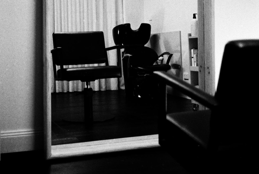 Black and white shot of an empty hair salon chair in front of a mirror.
